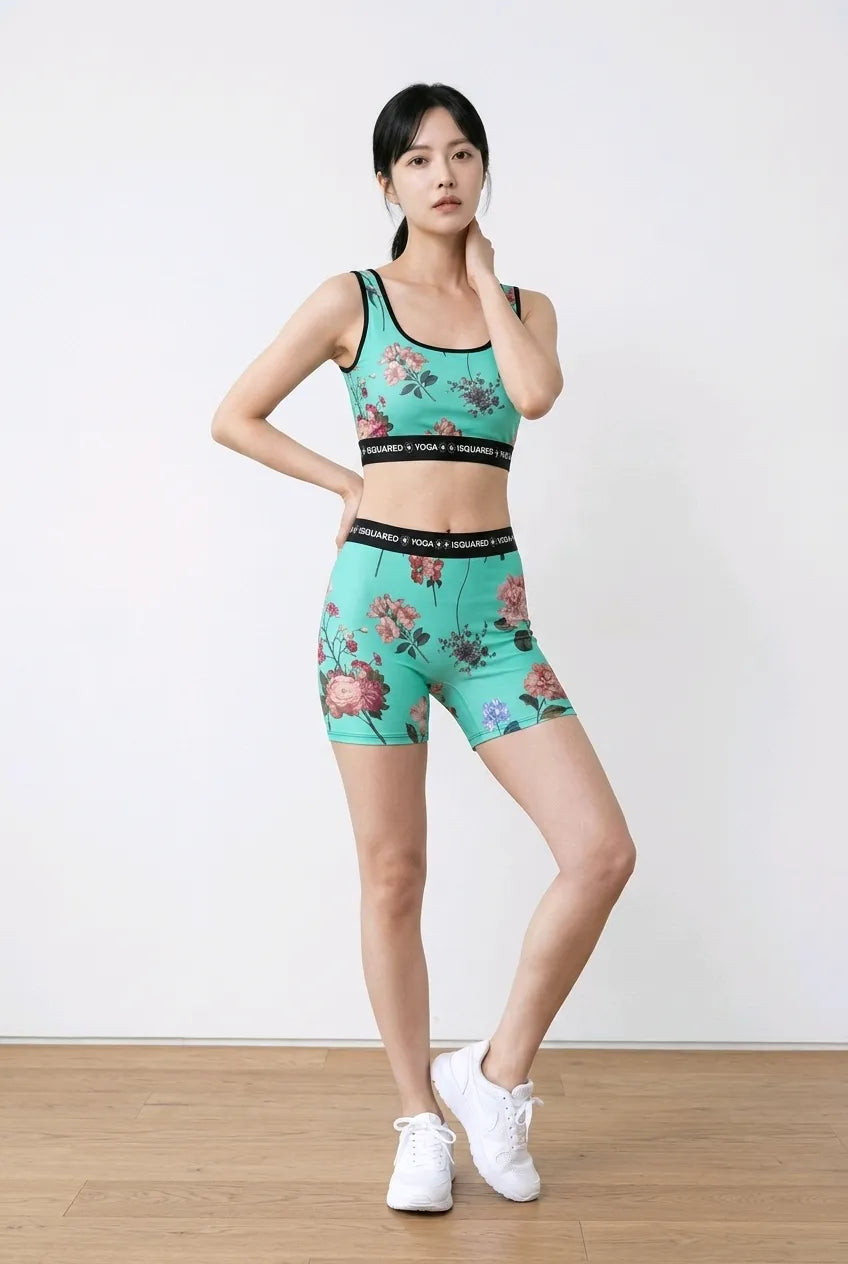 Vibrant turquoise yoga set with floral pattern, featuring a cropped tank top and matching shorts, styled with white sneakers.
