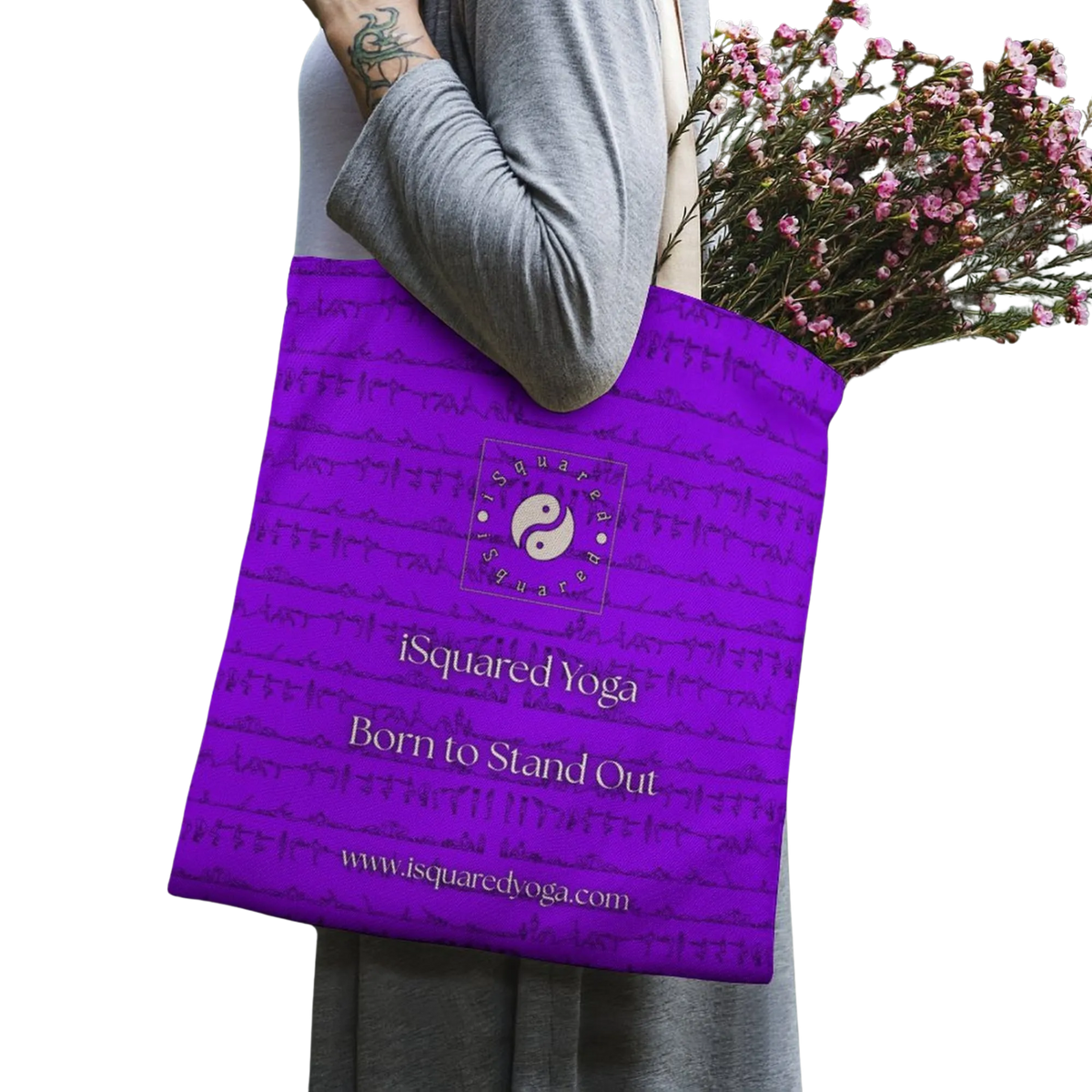 Purple tote bag with the iSquared Yoga logo, held by a person wearing a grey shirt, filled with flowers.