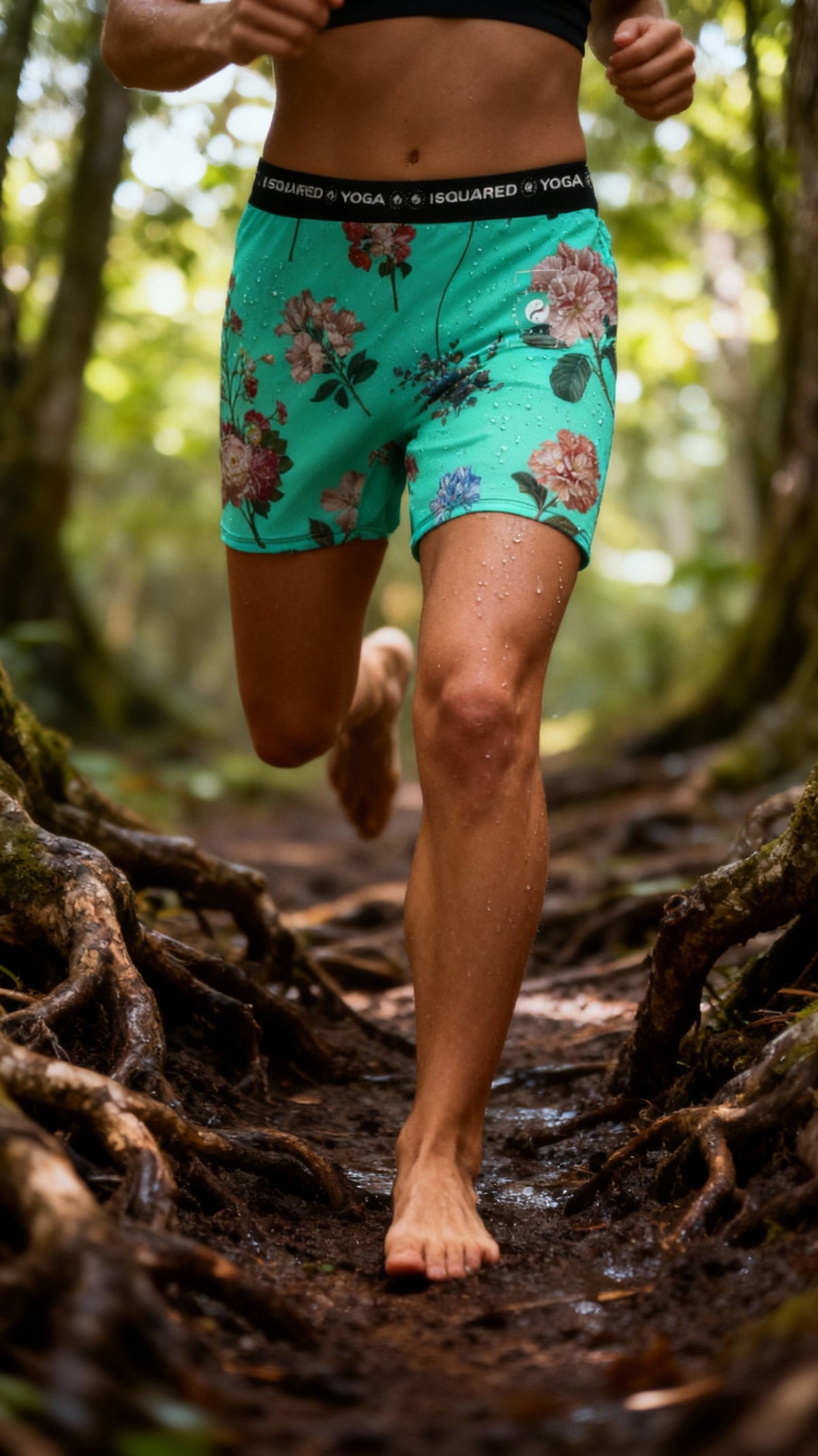 Vibrant turquoise iSquared Yoga Shorts with floral pattern, worn by a model running on a forest path, showing moisture beads.