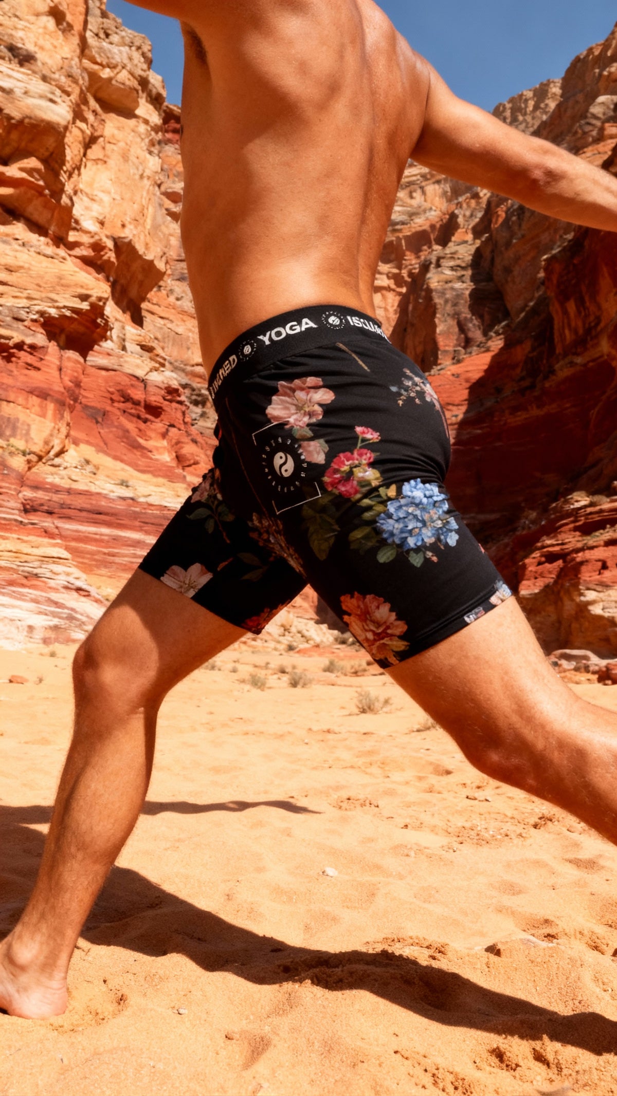 Black iSquared Yoga Shorts featuring a botanical floral print, worn by a model in a yoga pose on sandy terrain.