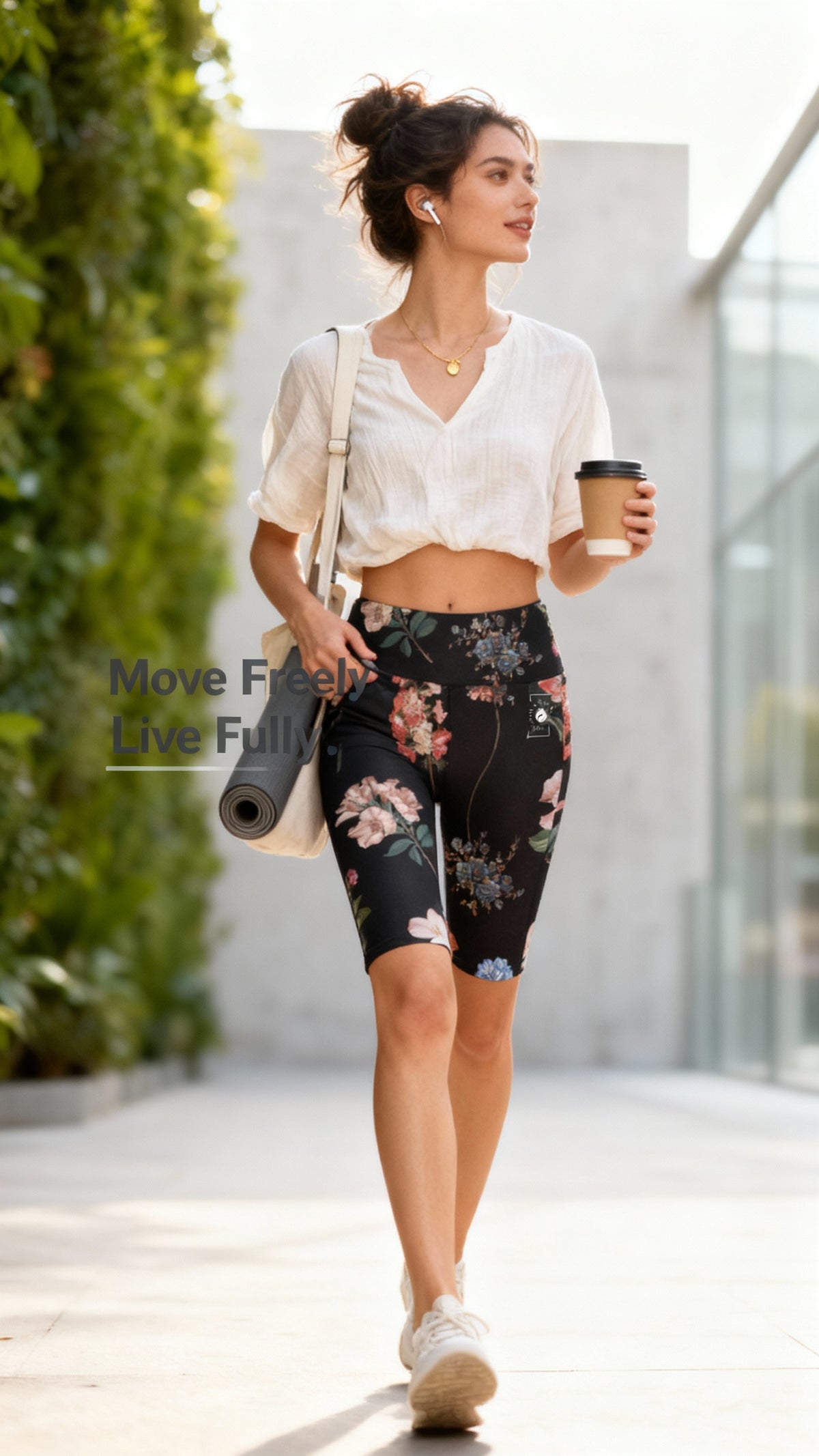 High-waisted black biker shorts with a floral pattern, worn with a cropped white shirt, carrying a yoga mat and coffee.